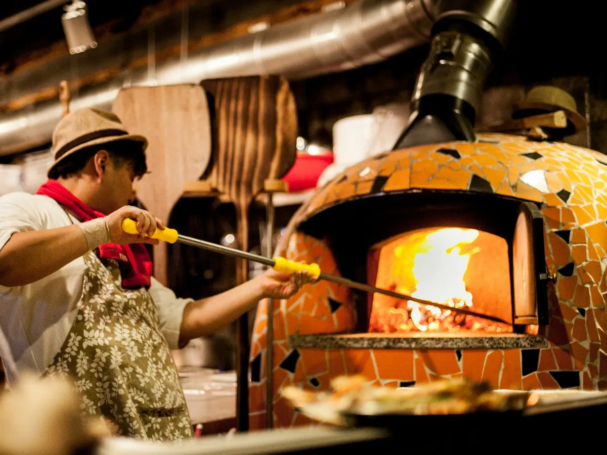Un pizzaïolo enfourne une pizza dans un four à bois.