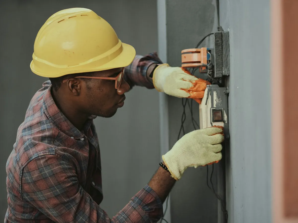 Un électricien en casque de chantier vérifie un tableau électrique.